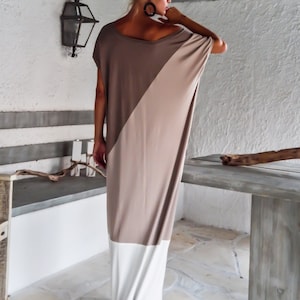 May include: A long, loose-fitting dress with a diagonal color block design. The top half of the dress is a light brown color, and the bottom half is white. The dress has short sleeves and a scoop neckline.