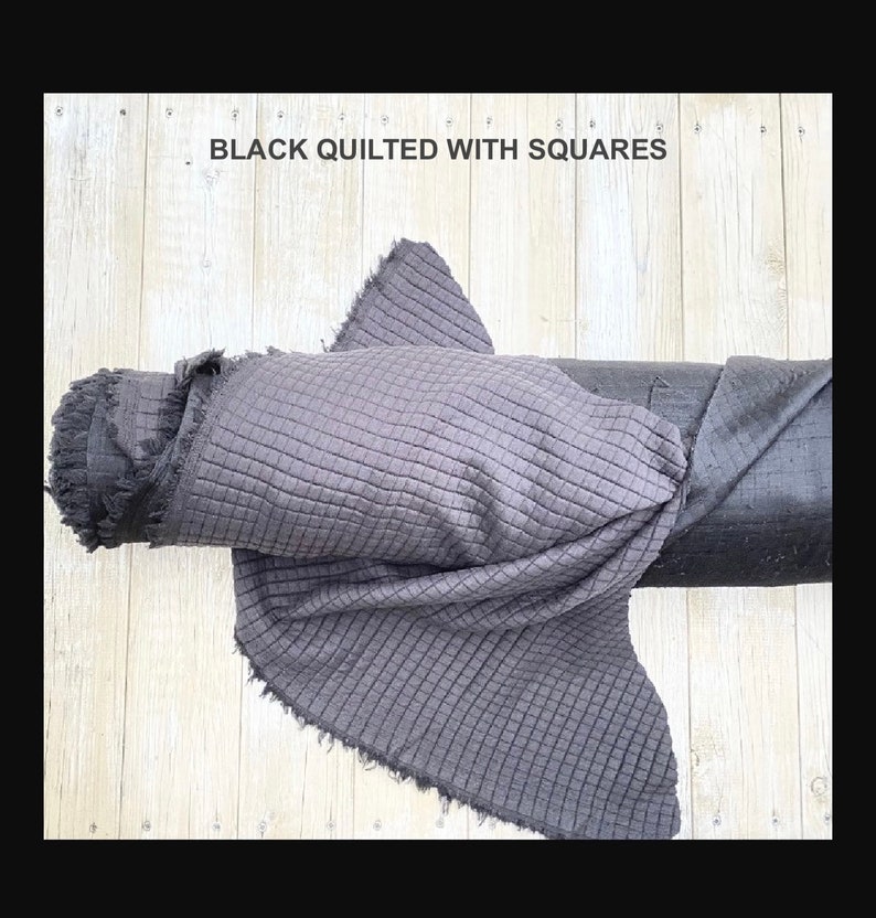 May include: Black quilted fabric with a square pattern. The fabric is rolled up and has a frayed edge.