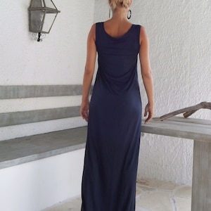 Puede incluir: Una mujer con un vestido largo de maxi sin mangas de color azul oscuro. El vestido tiene un escote redondo y un ajuste holgado.