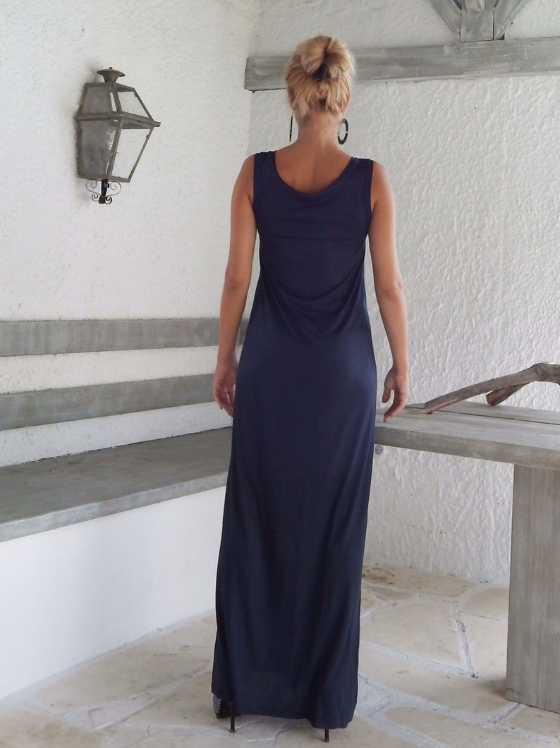 Puede incluir: Una mujer con un vestido largo de maxi sin mangas de color azul oscuro. El vestido tiene un escote redondo y un ajuste holgado.