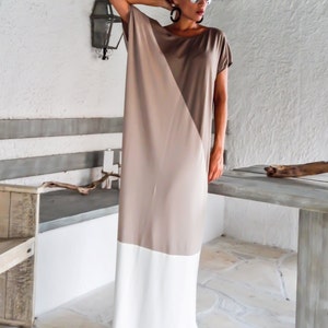 May include: A long, loose-fitting dress with a diagonal color block design. The top half of the dress is a light brown color, and the bottom half is white. The dress has short sleeves and a scoop neckline.