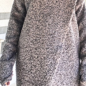 May include: A long-sleeved, gray and black sweater with a textured, fuzzy fabric. The sweater has a high neckline and a slightly asymmetrical hem.