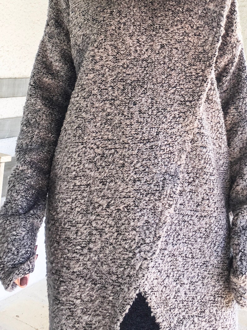 May include: A long-sleeved, gray and black sweater with a textured, fuzzy fabric. The sweater has a high neckline and a slightly asymmetrical hem.