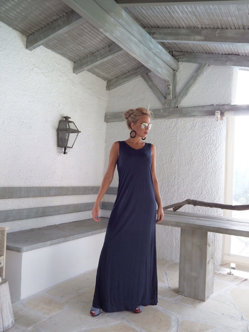 Puede incluir: Una mujer con un vestido largo azul oscuro sin mangas. Est&aacute; de pie en una habitaci&oacute;n con una mesa y un banco de madera.