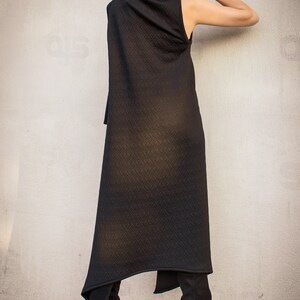 May include: A black sleeveless tunic with a high neck and a long, flowing design. The tunic is made of a textured fabric and has a slightly asymmetrical hemline.
