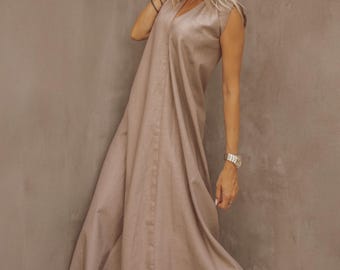 May include: A light brown, sleeveless dress with a V-neck and a flowing skirt. The dress is paired with light-colored high-heeled sandals and sunglasses. The model is wearing a silver watch and bracelets.