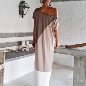 May include: A long, loose-fitting dress with a diagonal color block design. The top half of the dress is a light brown color, and the bottom half is a beige color. The dress has a white trim at the bottom.