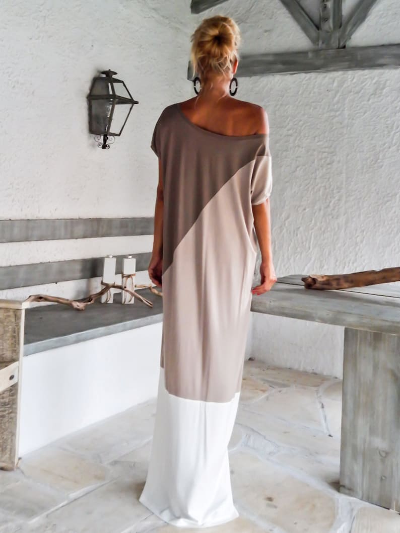 May include: A long, loose-fitting dress with a diagonal color block design. The top half of the dress is a light brown color, and the bottom half is a beige color. The dress has a white trim at the bottom.