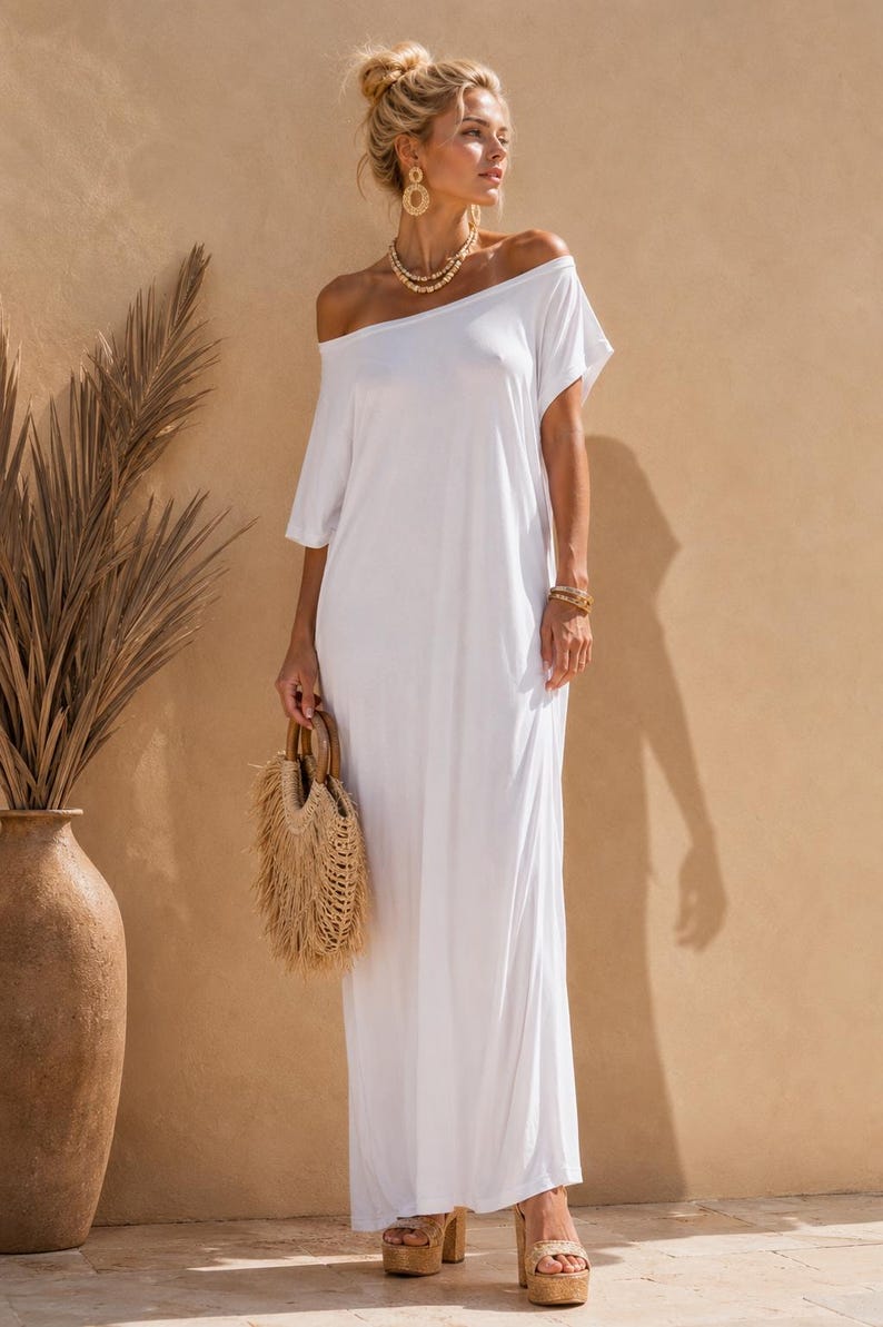 May include: A floor-length white maxi dress featuring an off-the-shoulder neckline and short sleeves. The garment is paired with a round straw handbag with wooden handles, gold-toned layered necklaces, gold earrings, and platform sandals.