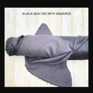 May include: Black quilted fabric with a square pattern. The fabric is rolled up and has a frayed edge.