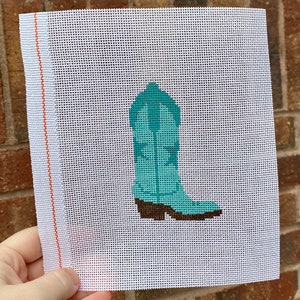May include: A white canvas with a turquoise cowboy boot design. The boot has a brown sole and heel.