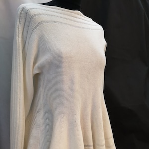 Puede incluir: Un suéter de punto blanco con cuello de barco y dobladillo acampanado. El suéter tiene un delicado patrón de tejido abierto.