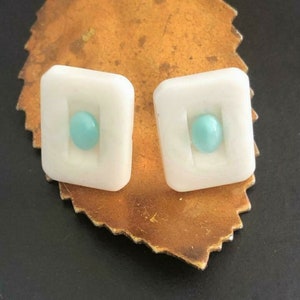 Puede incluir: Un par de pendientes cuadrados blancos con un círculo azul claro en el centro de cada uno.