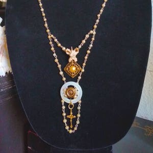 May include: A gold and white layered necklace with a cross pendant, a square button with a gold frame and a white pearl center, and a white circle with a gold button in the center.