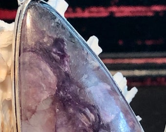 May include: A silver pendant with a teardrop-shaped purple and white stone. The stone has a swirling pattern and a glossy finish.