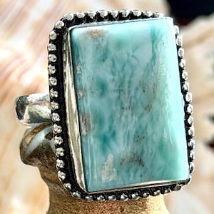 May include: A rectangular light blue and white stone ring set in a silver bezel with a beaded edge. The stone features a marbled pattern with varying shades of turquoise and white, held by a polished silver band with a smooth finish.