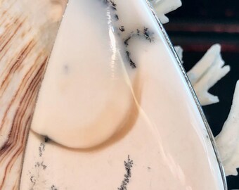 May include: A white and gray dendritic opal pendant with a silver bail. The opal has a smooth, polished surface and a teardrop shape.
