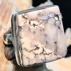 May include: A square-shaped ring with a white and grey stone set in a silver band. The stone has a marbled pattern.