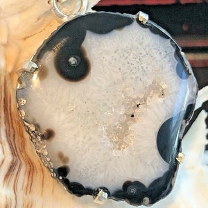 May include: A white agate pendant with black banding and a silver bail. The agate has a natural crystal formation in the centre.