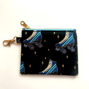 May include: A black zippered pouch with a gold zipper pull and a repeating pattern of blue and white roller skates on a black background with gold stars.