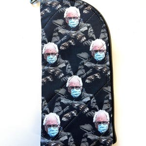 May include: A black zippered pouch with a quilted pattern featuring a repeated image of Bernie Sanders wearing a blue face mask.