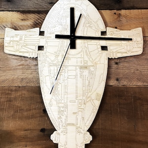 May include: A wooden wall clock shaped like the Star Wars character Boba Fett's spacecraft. The clock has black hands and a light wood finish.