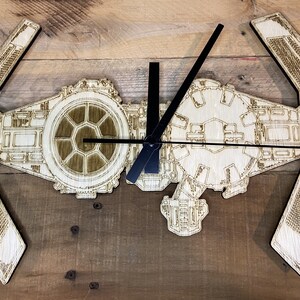 May include: A wooden clock shaped like a TIE fighter from Star Wars. The clock has black hands and a wood grain finish.