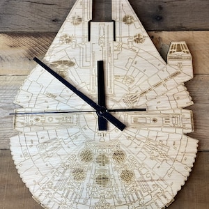May include: A wooden wall clock shaped like the Millennium Falcon from Star Wars. The clock has black hands and a detailed outline of the spaceship.