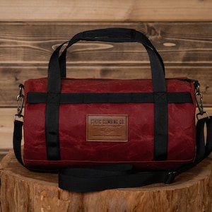 May include: A burgundy canvas duffel bag with black straps and a brown leather patch that reads "STATIC CLIMBING CO."