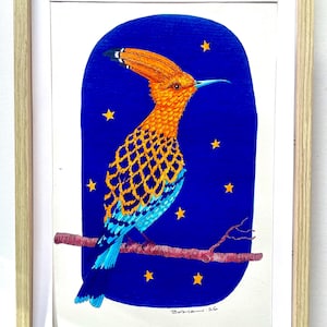 May include: Framed artwork featuring a colorful bird illustration. The bird has orange and blue plumage, perched on a branch against a dark blue background with yellow stars. The artwork is signed and framed in a light wood frame.