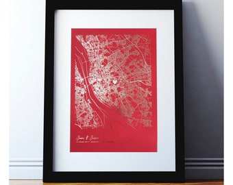 May include: A framed print of a city map with a silver heart marking a location. The map is on a red background and the text "James & Jessica 12 August 2017" is printed below the map.