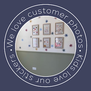 May include: A wall decorated with framed children's artwork and star-shaped stickers in various colors. The artwork is displayed on a white wall with a green lower section. The text "We love customer photos. Kids love our stickers" is in a circular design.