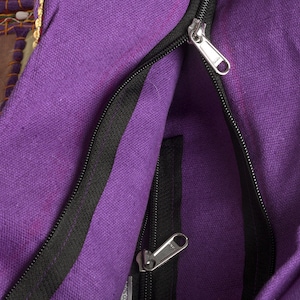 May include: A purple canvas bag featuring a main zippered compartment and an additional interior zippered pocket. The bag is constructed with a textured fabric and includes silver-toned metal zipper pulls for both the main opening and the inner pocket.