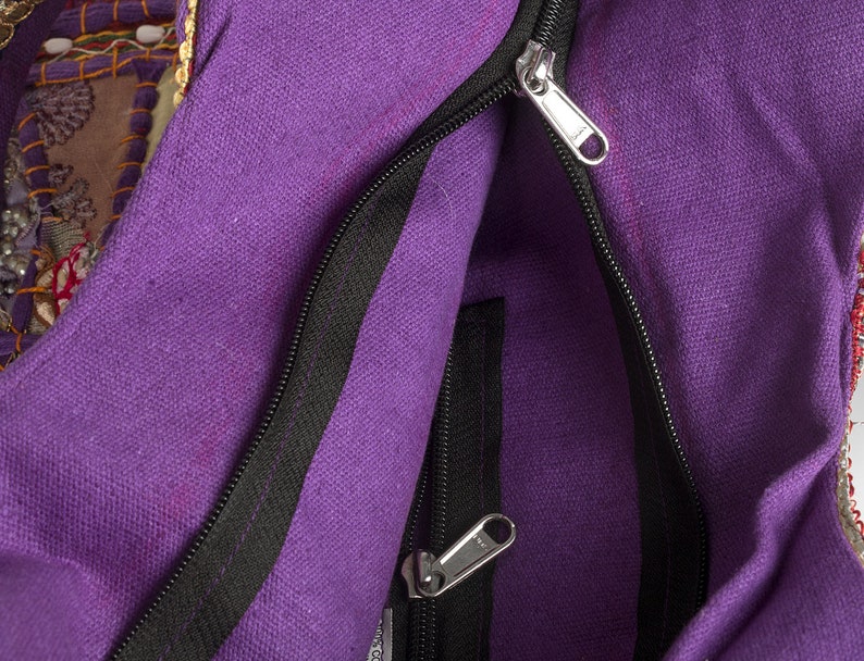 May include: A purple canvas bag featuring a main zippered compartment and an additional interior zippered pocket. The bag is constructed with a textured fabric and includes silver-toned metal zipper pulls for both the main opening and the inner pocket.