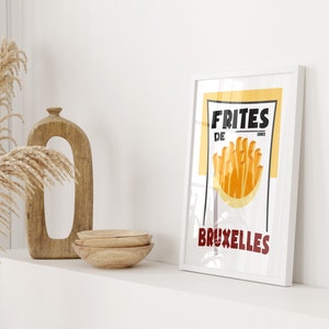 Puede incluir: Un p&oacute;ster enmarcado blanco con fondo amarillo y texto negro que dice "FRITES DE BRUXELLES". El p&oacute;ster presenta un gr&aacute;fico de papas fritas en una bolsa de papel.