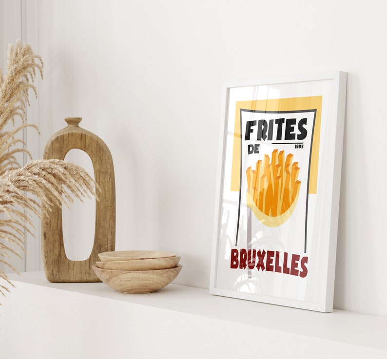 Puede incluir: Un p&oacute;ster enmarcado blanco con fondo amarillo y texto negro que dice "FRITES DE BRUXELLES". El p&oacute;ster presenta un gr&aacute;fico de papas fritas en una bolsa de papel.