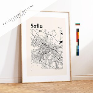 May include: A framed wall art print featuring a black and white street map of Sofia, Bulgaria. The map is set against a light cream background with the text Sofia and Bulgaria printed at the top. A vertical color palette bar is visible.