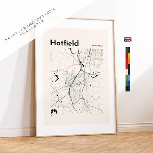May include: A vertical rectangular wall art print featuring a black line map of Hatfield, Hertfordshire on a light beige background. The text Hatfield and Hertfordshire are printed in black. The print is enclosed in a thin wooden frame.
