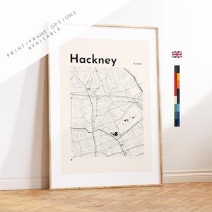 May include: A framed wall art print featuring a minimalist black and white street map of Hackney, London. The design includes the text Hackney and London in a bold sans-serif font against a light cream background, with thin black lines.