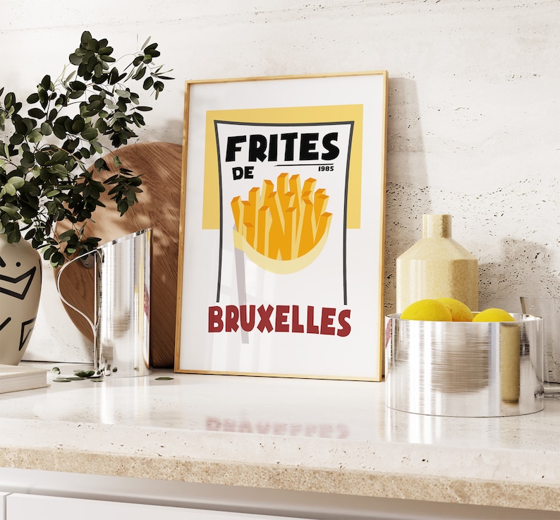 Puede incluir: Un p&oacute;ster de estilo vintage con fondo amarillo y texto negro que dice "Frites de Bruxelles" con una ilustraci&oacute;n de patatas fritas. El p&oacute;ster est&aacute; enmarcado en un marco dorado y est&aacute; colgado en una pared blanca.