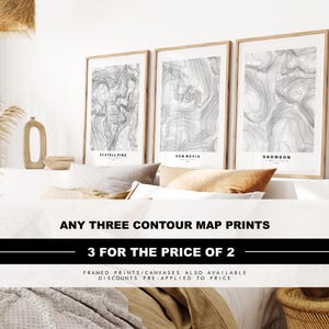 May include: Three vertical framed wall art prints featuring black and white topographic contour maps of Scafell Pike, Ben Nevis, and Snowdon. Each print displays detailed elevation lines and the mountain name in a clean, sans-serif font.