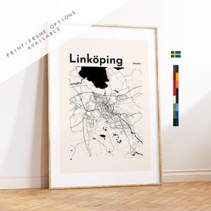 May include: A framed wall art print featuring a black and white map of Linköping, Sweden, with the text Linköping and Sweden printed at the top. The map displays intricate road networks and a large black water feature on a light beige background.