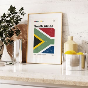 May include: A framed print with a vintage style graphic of the South African flag. The flag is red, yellow, green, black, and blue. The print is on a white background with the words "South Africa" and "162..." in black text.
