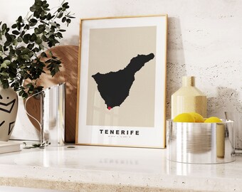 Pode incluir: Uma impressão emoldurada de uma silhueta preta da ilha de Tenerife, com a palavra "Tenerife" impressa abaixo da imagem. A impressão está sobre um fundo bege e é emoldurada em uma moldura de madeira clara. A impressão está sentada em uma bancada branca com um jarro de prata e uma tigela de limões no fundo.