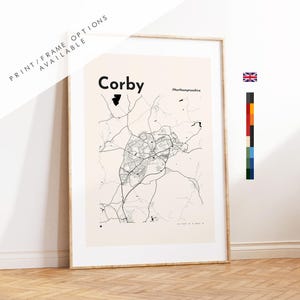 May include: A framed print of a map of Corby, Northamptonshire, in black and white. The map shows the road network and town layout. The print is displayed in a wooden frame, with the text "PRINT/FRAME OPTIONS AVAILABLE" at the top.