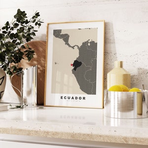 May include: A framed print of a map of Ecuador with the country highlighted in black. The map is on a beige background with the word "ECUADOR" printed in black at the bottom of the frame.