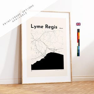 May include: A framed wall art print featuring a minimalist map of Lyme Regis, Dorset. The design displays black line work for roads and a solid black shape for the coastline against a light cream background. The text reads Lyme Regis and Dorset.