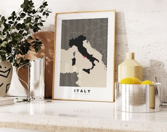 May include: A framed map of Italy with a gold frame. The map is in black and beige with a red dot marking a location. The word "ITALY" is printed at the bottom of the map.