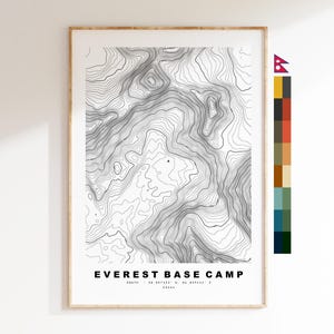 May include: A framed topographic map print titled EVEREST BASE CAMP, featuring black contour lines on a white background. The text includes coordinates 28.007222 N, 86.859444 E and 5364m. A vertical color palette strip is positioned to the right of the print.