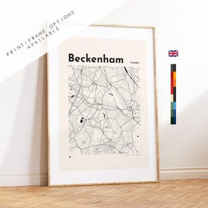 Op de afbeelding: Een ingelijste wandkunstprint met een zwart-witte stadsplattegrond van Beckenham, Londen. De kaart staat op een lichtcrèmekleurige achtergrond met de tekst Beckenham en /London bovenaan. De lijst heeft een lichte houtkleur.
